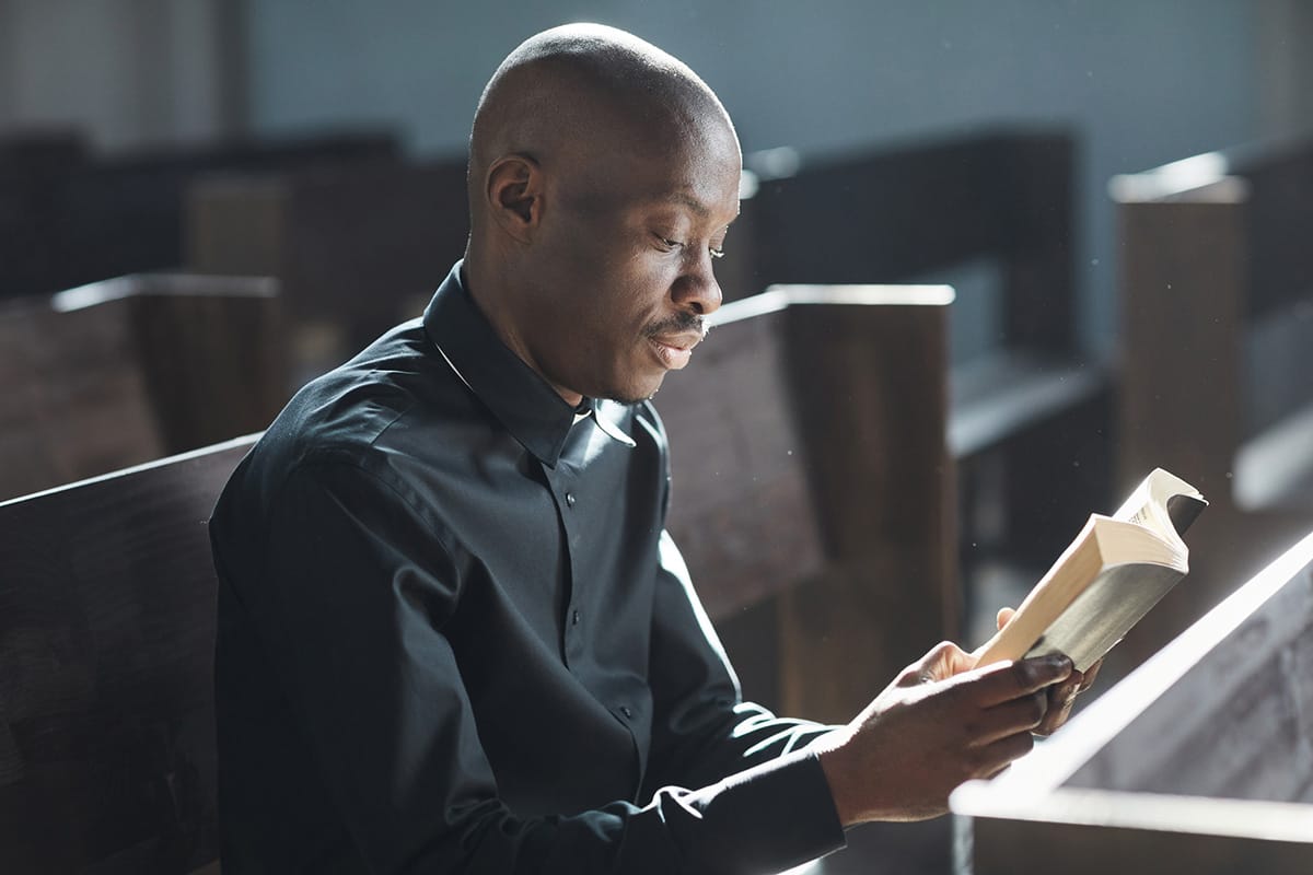 African-American ordained online minister reading the Bible while seated in empty church pews