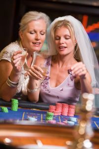 Woman in bridal veil with another woman in casino playing roulette and smiling (selective focus)