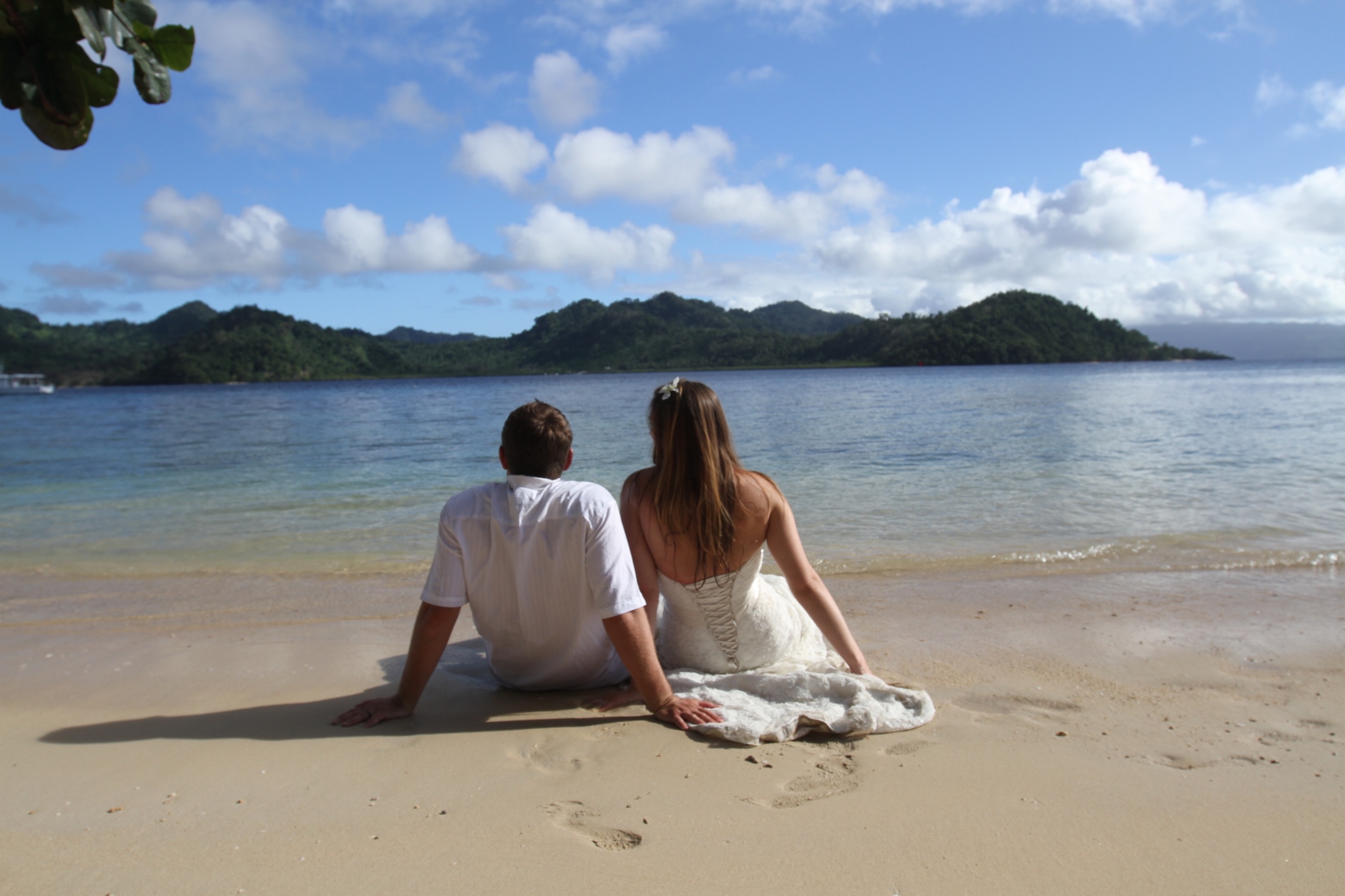 An eloping couple sitting together on a beach.