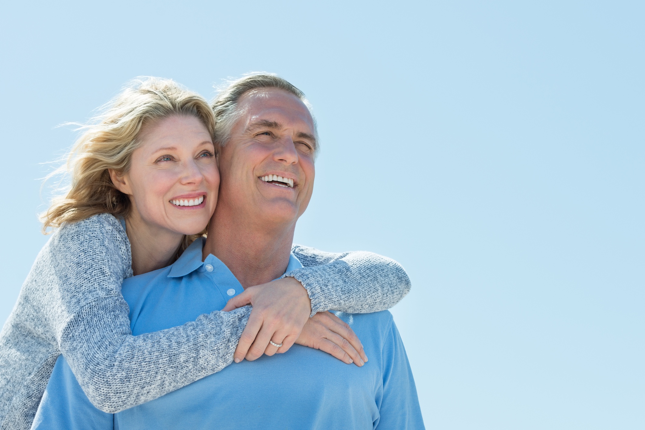 Woman Embracing Man From Behind While Looking Away Against Sky