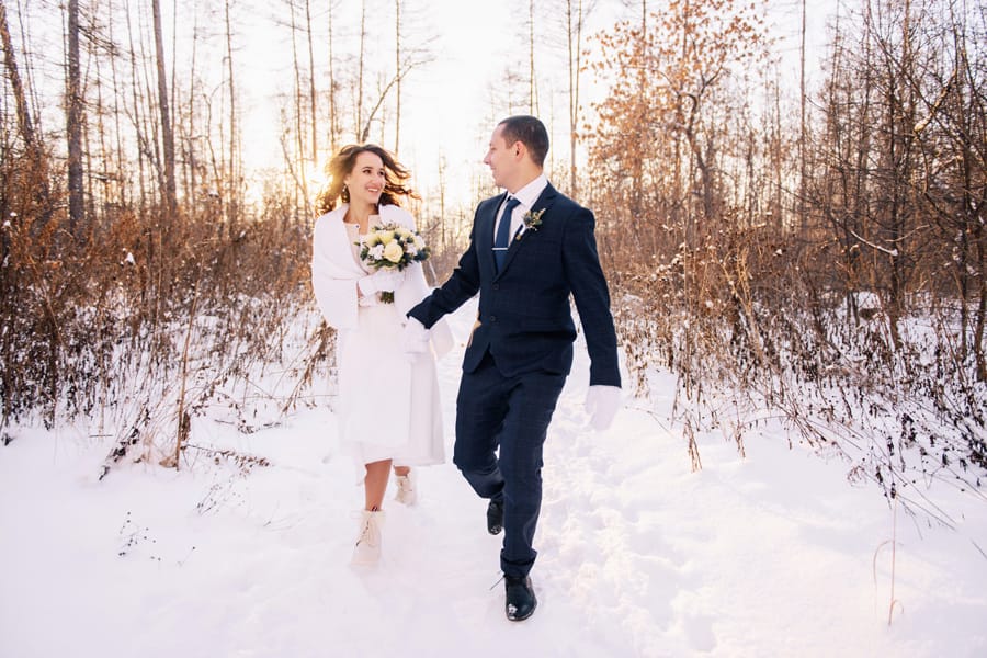 Happy bride and groom walking through snow after Christmas themed wedding