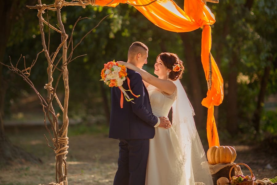 Couple embracing under wedding arch at fall wedding